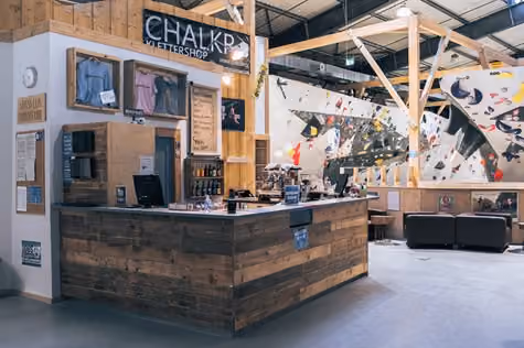 Moderner Empfangstresen im Chalkr Klettershop mit Blick auf eine Kletterwand, Innenraum, Tag.