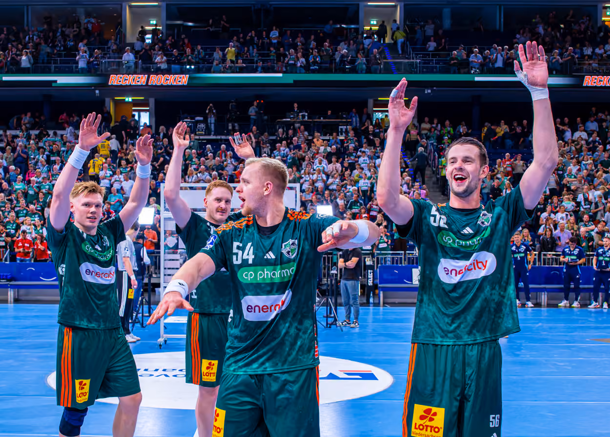 Handballspieler jubeln nach einem Spiel auf dem Spielfeld vor Zuschauern in der Halle