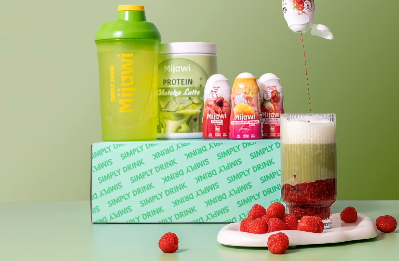 Protein powder, shaker, and raspberries arranged with a green matcha latte being prepared in a glass.