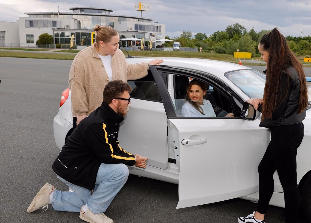 Vier Personen bei einem Fahrtraining auf einem offenen Übungsgelände an einem bewölkten Tag.