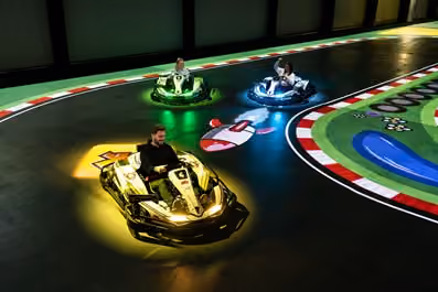 Drei Personen fahren abends in einer beleuchteten Indoor-Kartbahn um die Wette.