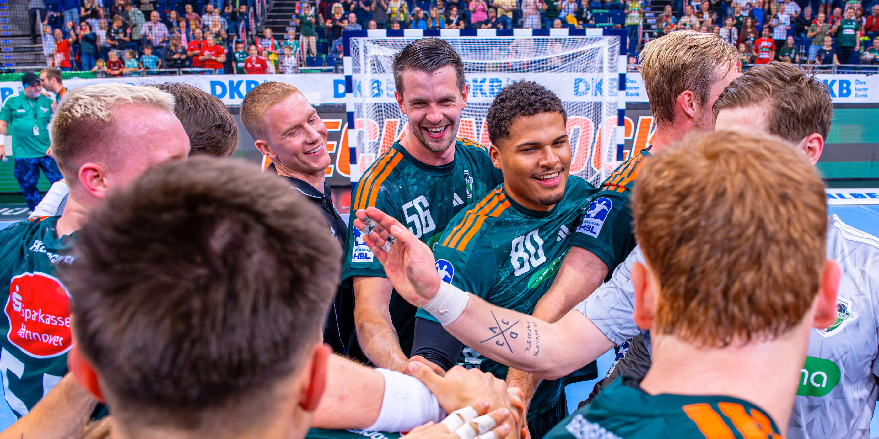 Handballspieler feiern ihren Sieg bei einem Spiel in der Halle vor begeistertem Publikum.