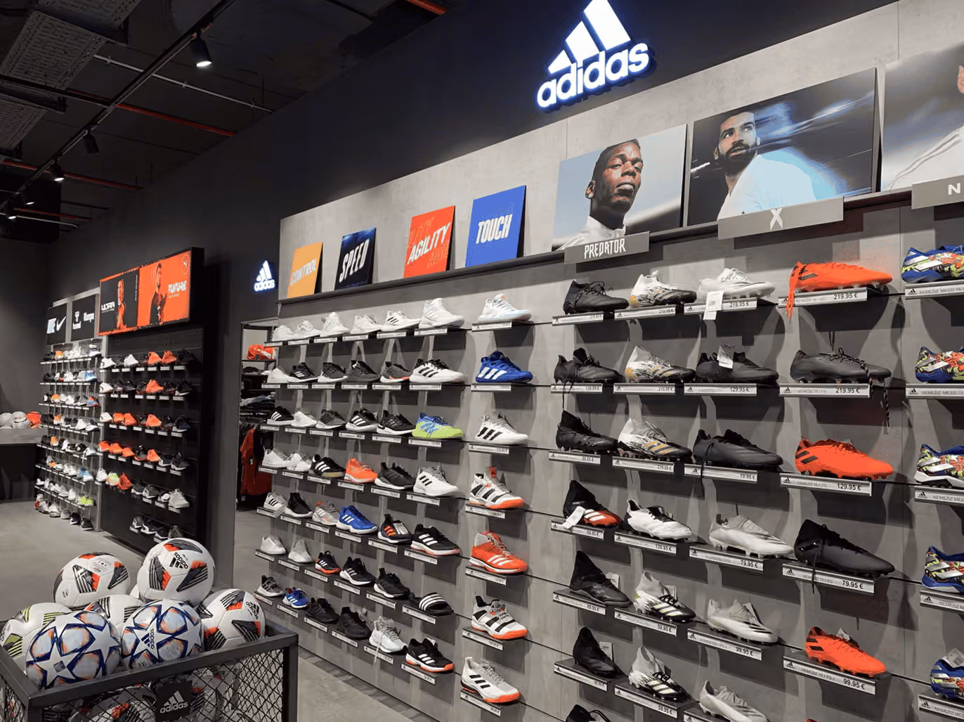 Moderne Adidas-Fußballschuhe und Bälle im Geschäft, präsentiert an einer Wand im Innenraum.