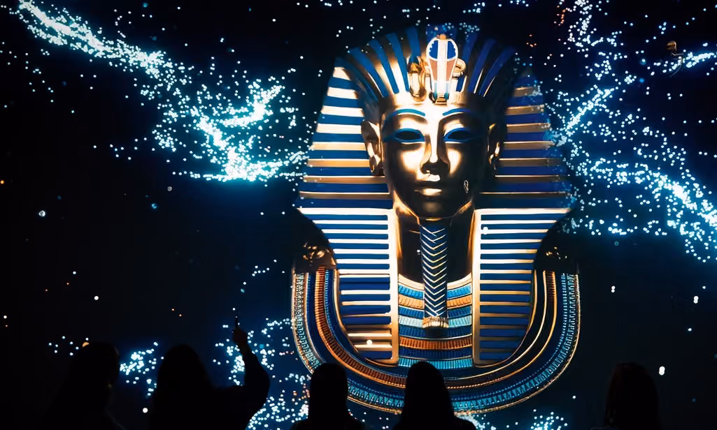 Besucher betrachten 2024 in einer Ausstellung eine leuchtende Maske des Pharaos Tutanchamun.