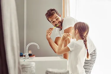 Ein Vater putzt sich gemeinsam mit seiner Tochter am Waschbecken die Zähne. 