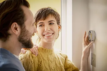 Ein junges Pärchen stellt die Temperatur mit einem smarten Raumthermostat ein. 