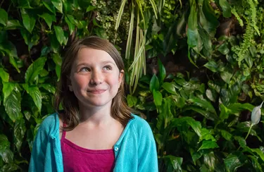 Mädchen steht vor einer begrünten Fassade.