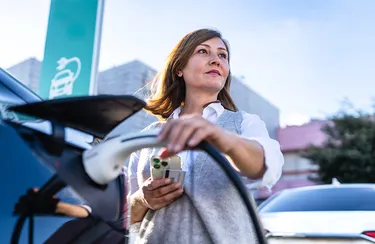 Eine Frau lädt ein schwarzes Elektroauto an einer Ladesäule. 