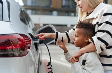 Eine Mutter und ihr Sohn laden das E-Auto auf einem Parkplatz.