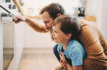Energiesparend backen und kochen. Ein Vater beobachtet mit seinem Sohn das Garen der Speisen im Backofen.