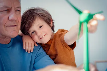 Lächelnder Junge, der mit seinem Großvater zu Hause das Modell einer Windenergieanlage betrachtet.