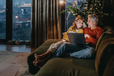 Vater und Tochter sitzen auf dem Sofa und schauen sich zusammen ei-nen Film auf dem  Laptop an. 