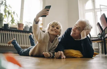Großvater und Enkel liegen im Wohnzimmer auf dem Boden und machen ein Selfie.