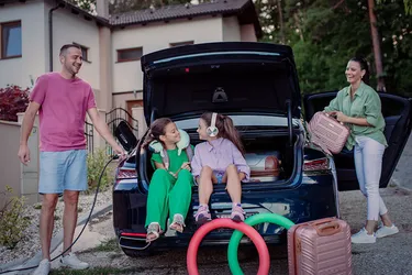 Ein Familienvater lädt zuhause das E-Auto auf. Die Kinder sitzen währenddessen im Kofferraum. 