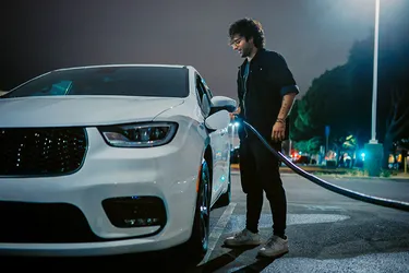 Ein Mann steht an seinem E-Fahrzeug und lädt es auf.