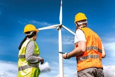 Zwei Windkrafttechniker:innen inspizieren eine Windenergieanlage