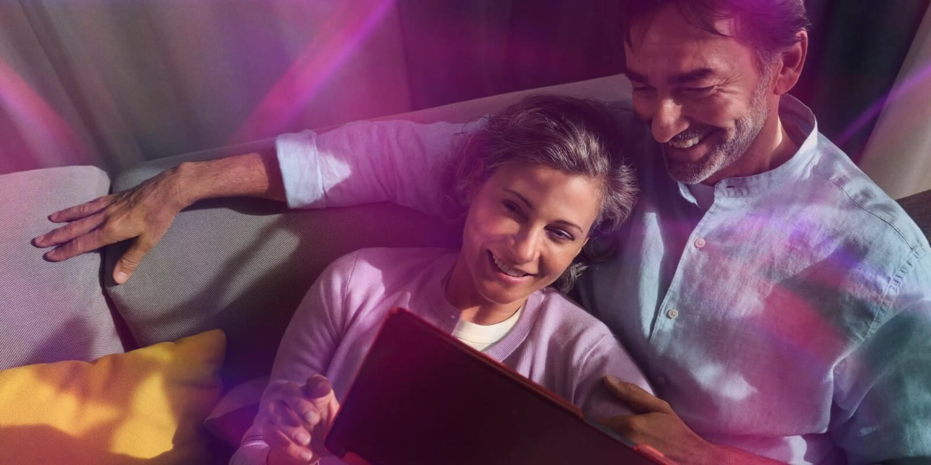 Mann und Frau liegen auf dem Sofa und schauen auf ein Tablet