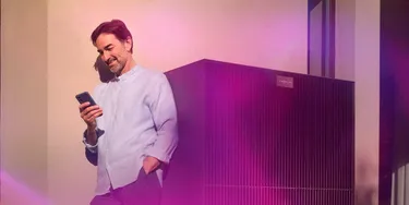 Man lehnt an Wärmepumpe und schaut auf sein Handy