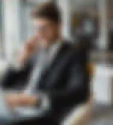 Ein Mann im Anzug sitzt vor einem Laptop und telefoniert mit seinem Smartphone