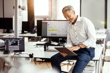 Ein Mann sitzt auf einem Schreibtisch und schaut auf sein Tablet