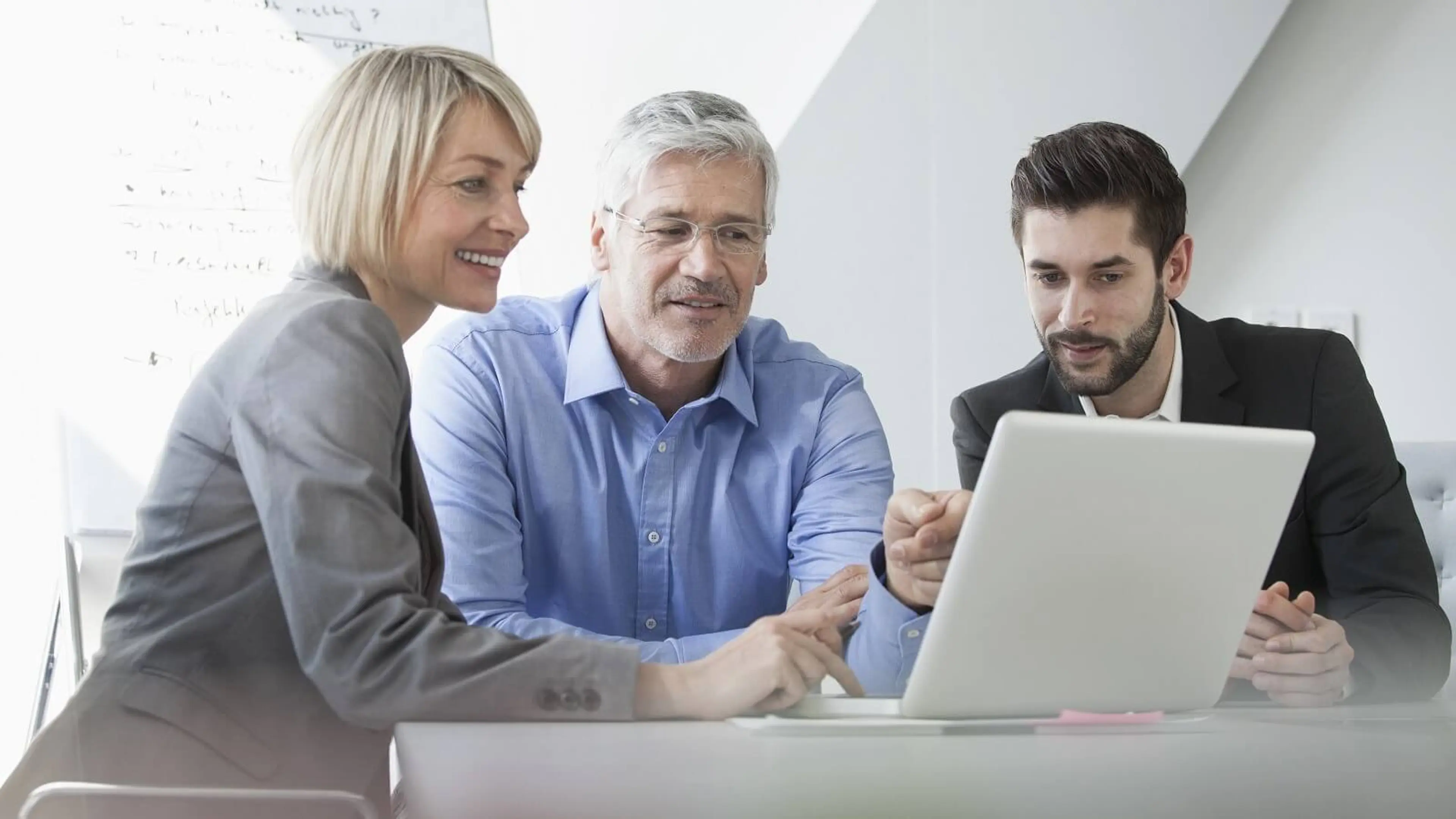 Frau und 2 Männer in Business-Kleidung schauen auf ein Laptop