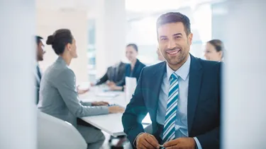 Mann im Anzug sitzt im Büro und lacht in die Kamera