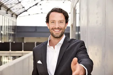 Mann lacht in die Kamera und streckt die Hand entgegen