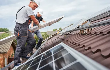 Nahaufnahme zweier Installateure die eine Photovoltaikanlage auf einem Hausdach installieren