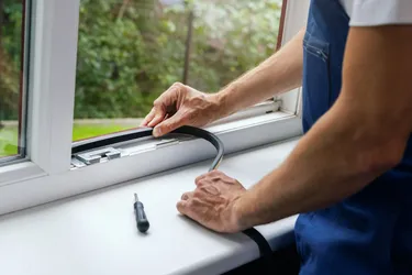 Nahaufnahme der Hände eines Handwerkers der ein Fenster mit einem Dichtungsband abdichtet