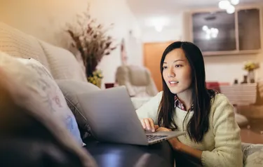 Eine junge Frau sitzt an einem Laptop in ihrem Wohnzimmer
