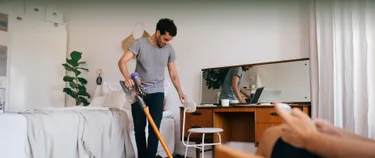 Das Bild zeigt einen Mann, der im Schlafzimmer staubsaugt.