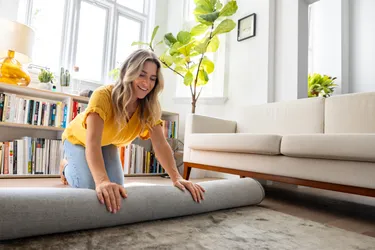 A woman rolls up a carpet in a living room 