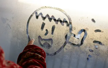 Nahaufnahme eines Kindes das mit seinem Finger ein lachendes Gesicht auf eine beschlagene Fensterscheibe malt