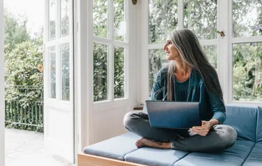 Eine Frau sitzt auf dem Sofa vor dem geöffneten Fenster