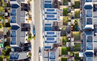 Die mit einer Vielzahl von Photovoltaikanlagen ausgestatteten Dächer einer modernen Wohnsiedlung aus der Vogelperspektive