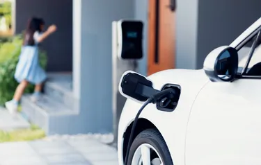 Nahaufnahme eines vor einem Haus stehenden Elektroautos, das an einer Wallbox hängt