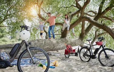 Eine junge Familie mit einer kleinen Tochter verbringt eine glückliche Zeit am Strand Neben einer Picknickdecke sind auch Sandspielzeug mit Förmchen und Eimern sowie zwei Elektroräder zu sehen
