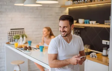 Ein Mann steht in einer Küche und hält ein Smartphone in seinen Händen