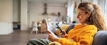 Frau sitzt mit dem Handy auf dem Sofa