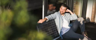 Ein Mann sitzt am Fenster neben einem Solarmodul.