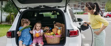 Frau lädt ein E-Auto mit geöffnetem Kofferraum