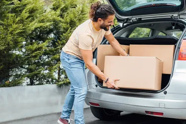 Ein Mann lädt Umzugskisten in den Kofferraum eines Autos