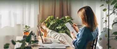 Eine Frau legt ihre Füße auf ihren Schreibtisch und zeichnet mit einem Bleistift auf weißem Papier.