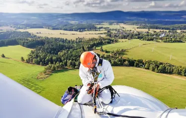 Nahaufnahme eines Monteurs der in schwindelnder Höhe auf der Gondel einer Windenergieanlage kniet