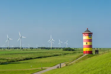 Landschaftsaufnahme mit einigen Windenergieanlagen und einem rot-gelb-gestreiften Leuchtturm.