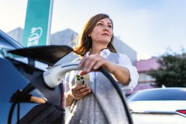 Nahaufnahme einer Frau die ein schwarzes Elektroauto an einer Ladesäule lädt