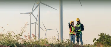 Mechaniker:innen stehen vor Windkraftanlagen in der Natur