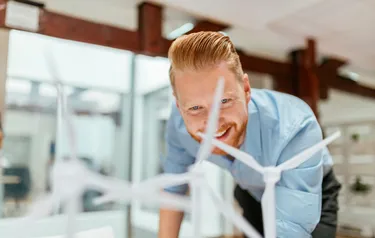 Ein Mann beugt sich lächelnd über ein auf einem Tisch stehendes Modell eines Windparks