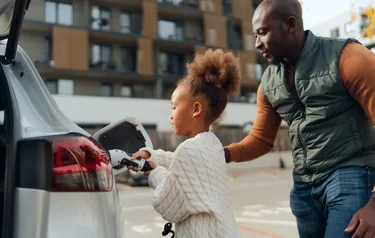 Ein Mann hilft einem kleinen Mädchen beim Laden eines Elektroautos