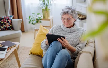 Eine Frau sitzt mit einem Ipad in der Hand auf dem Sofa